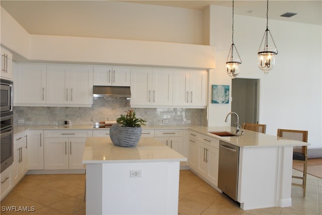 kitchen featuring decorative light fixtures, backsplash, stainless steel appliances, and a kitchen island with sink