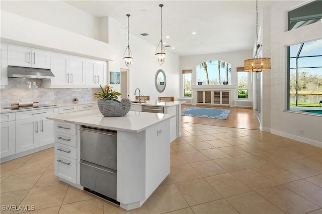 kitchen featuring pendant lighting, white cabinetry, backsplash, a kitchen island with sink, and black electric stovetop