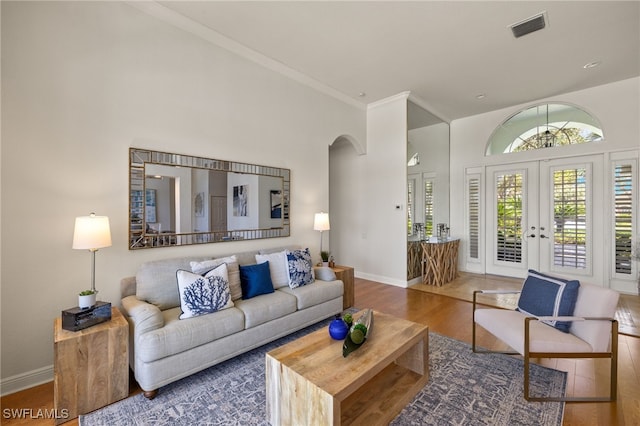 living room with arched walkways, wood finished floors, visible vents, baseboards, and crown molding