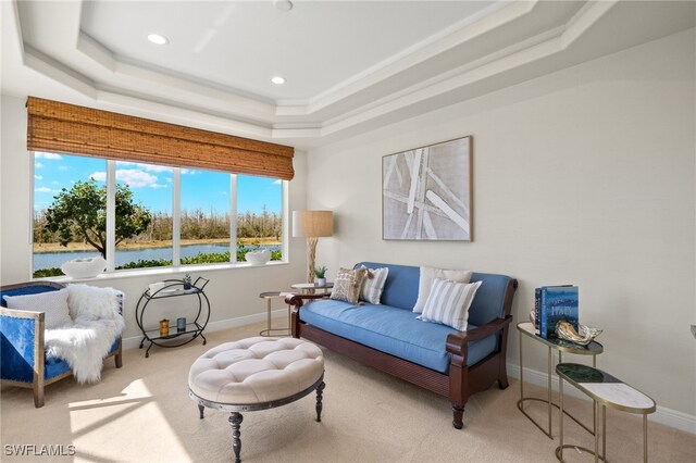 sitting room with carpet floors, a tray ceiling, a water view, and baseboards