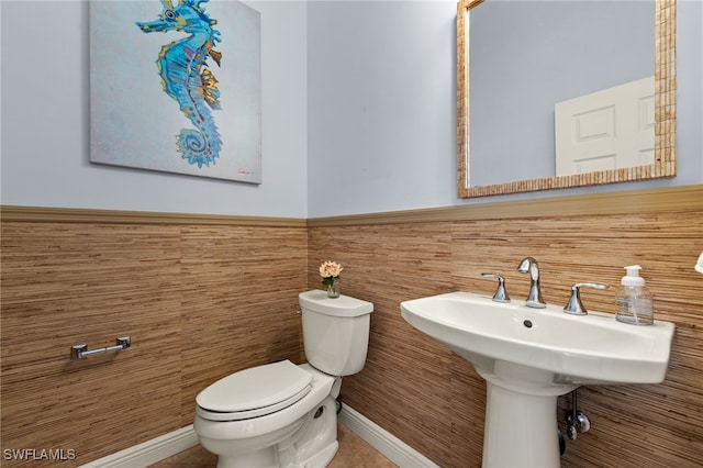 half bathroom featuring toilet, a sink, and wainscoting