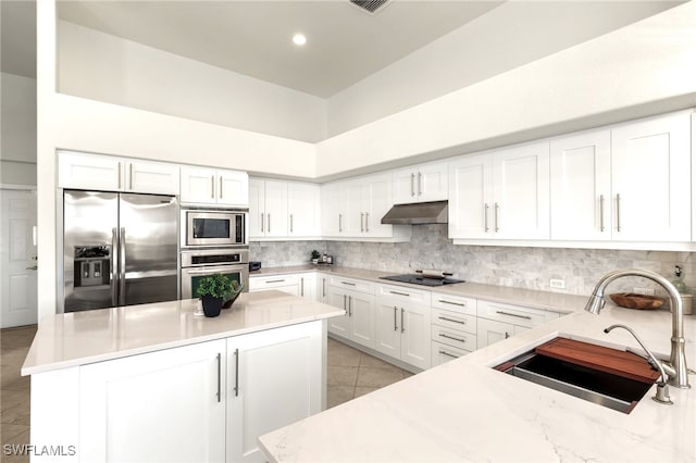 kitchen with tasteful backsplash, stainless steel appliances, under cabinet range hood, a sink, and light tile patterned flooring