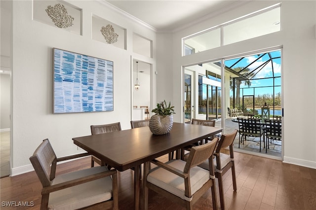 dining area featuring a high ceiling, wood finished floors, a sunroom, baseboards, and crown molding