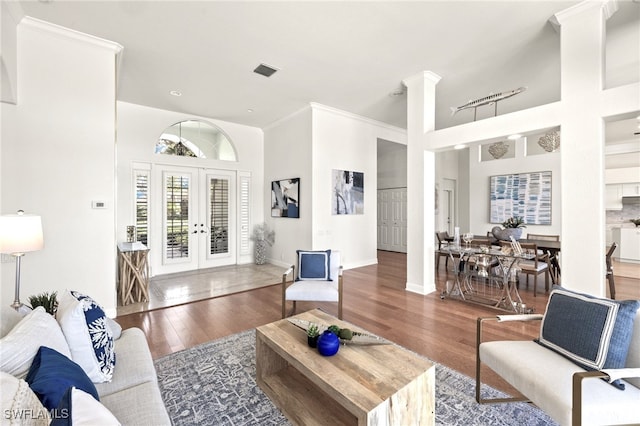 living room featuring wood finished floors, visible vents, french doors, ornate columns, and crown molding