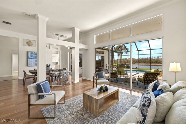 living room with a high ceiling, wood finished floors, visible vents, a sunroom, and baseboards