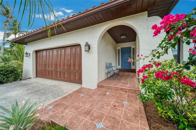 entrance to property with concrete driveway, an attached garage, and stucco siding