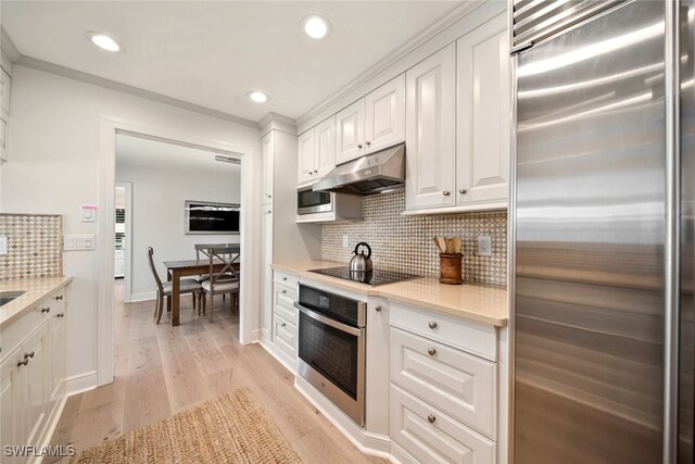 kitchen featuring ornamental molding, white cabinetry, light wood-type flooring, built in appliances, and decorative backsplash