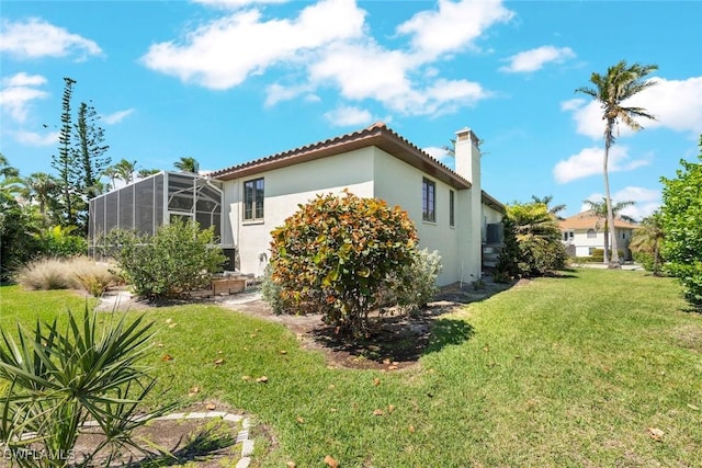 view of side of property featuring a lawn, a tile roof, a chimney, a lanai, and stucco siding