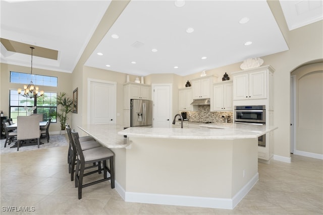 kitchen with a large island with sink, a breakfast bar, light stone counters, appliances with stainless steel finishes, and an inviting chandelier