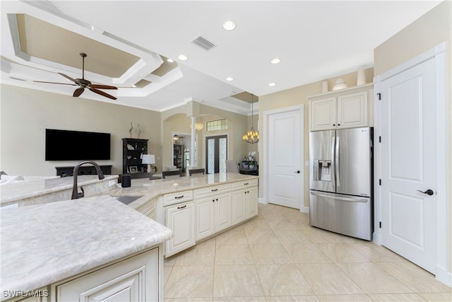 kitchen with ceiling fan with notable chandelier, sink, crown molding, light stone countertops, and stainless steel fridge