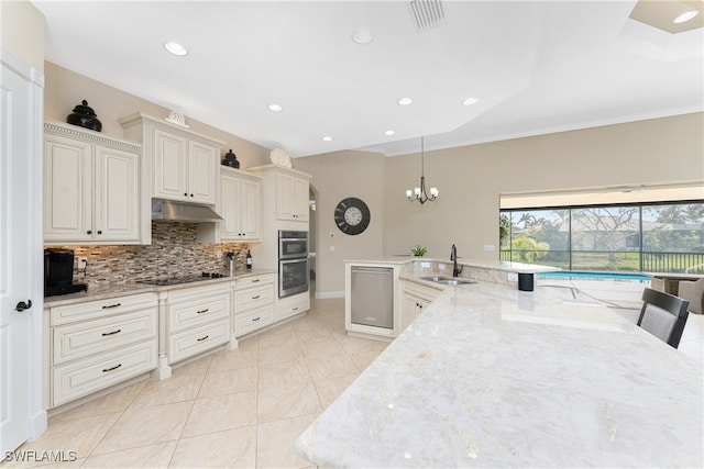 kitchen with sink, light stone counters, tasteful backsplash, black electric stovetop, and pendant lighting