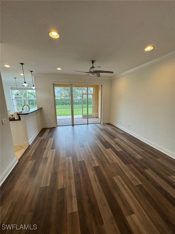 unfurnished living room featuring dark wood-type flooring, sink, ceiling fan, and crown molding