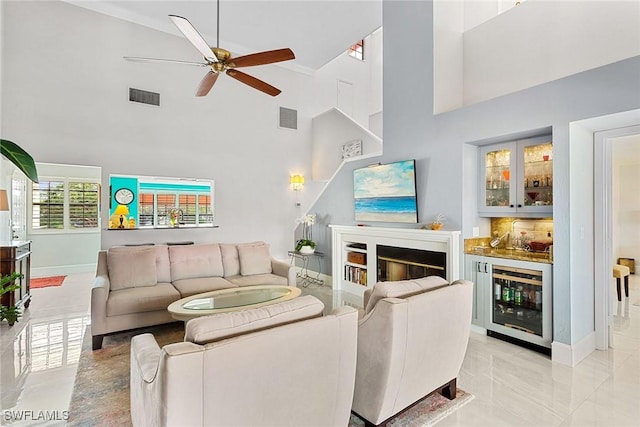 living room with ceiling fan, indoor bar, beverage cooler, and a towering ceiling