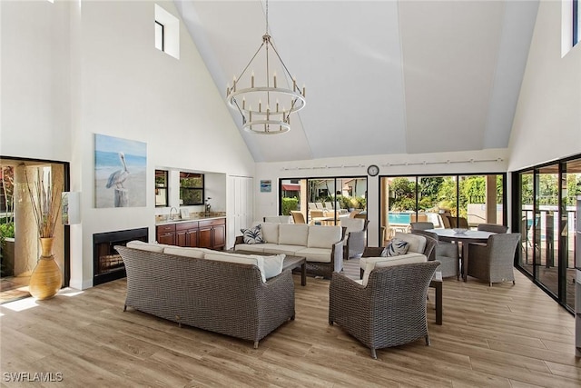 living room with an inviting chandelier, a towering ceiling, sink, and light hardwood / wood-style floors