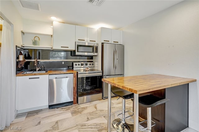 kitchen featuring white cabinets, a kitchen breakfast bar, sink, appliances with stainless steel finishes, and butcher block countertops