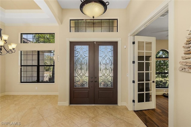 tiled foyer entrance featuring french doors, crown molding, and a notable chandelier