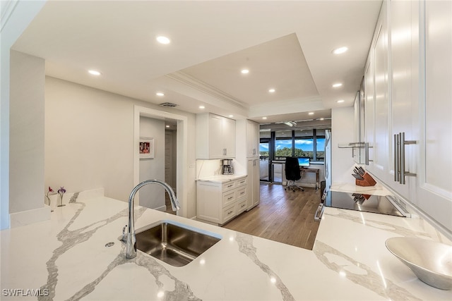 kitchen featuring black electric stovetop, light wood-type flooring, white cabinetry, light stone countertops, and sink