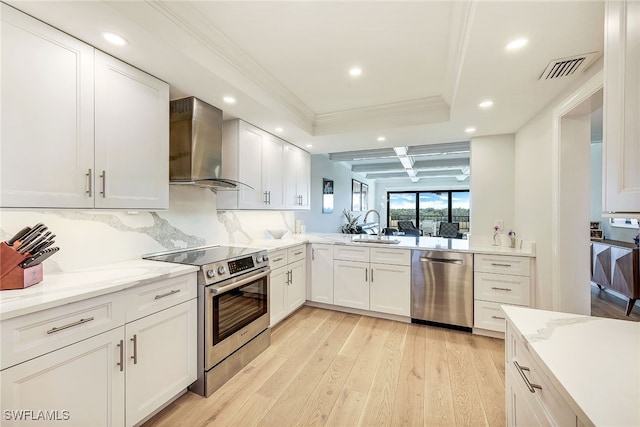 kitchen featuring stainless steel appliances, light hardwood / wood-style floors, sink, wall chimney range hood, and white cabinetry