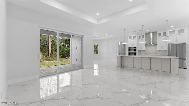 kitchen featuring a large island, stainless steel refrigerator, white cabinets, wall chimney range hood, and pendant lighting