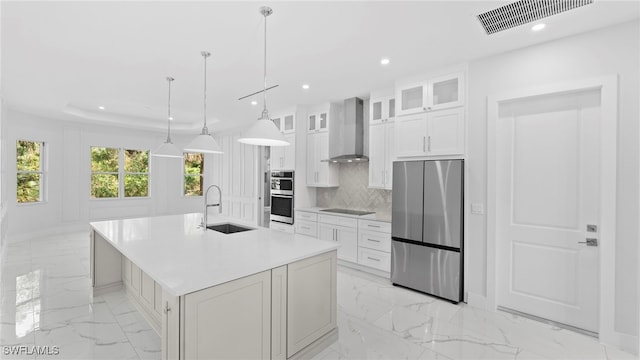 kitchen with a center island with sink, sink, white cabinetry, appliances with stainless steel finishes, and wall chimney exhaust hood