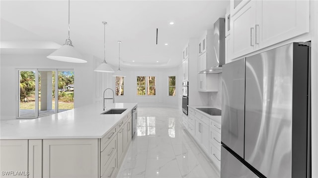 kitchen featuring white cabinetry, sink, appliances with stainless steel finishes, wall chimney exhaust hood, and pendant lighting