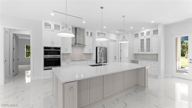 kitchen featuring stainless steel appliances, white cabinetry, hanging light fixtures, a spacious island, and wall chimney range hood