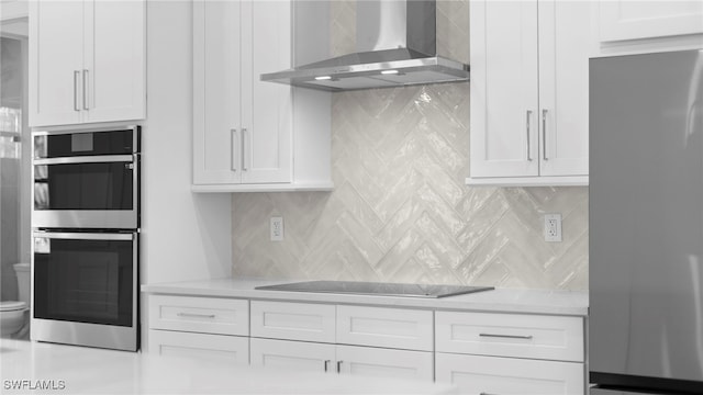 kitchen with stainless steel appliances, wall chimney range hood, and white cabinets