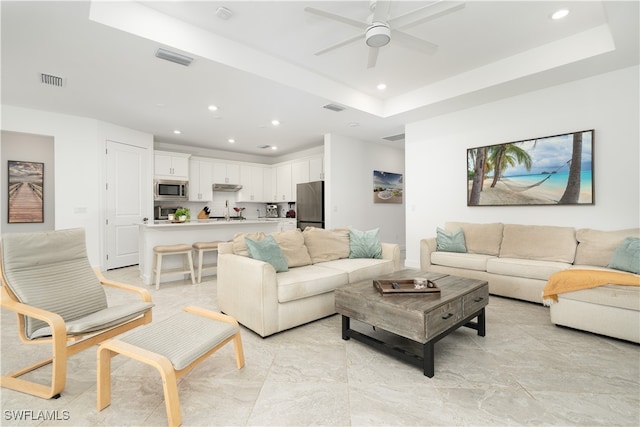 living room with ceiling fan, a raised ceiling, and sink