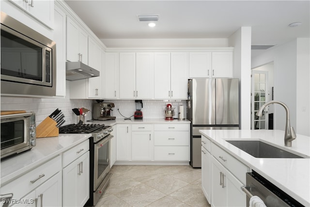 kitchen with stainless steel appliances, light tile patterned flooring, sink, backsplash, and white cabinets