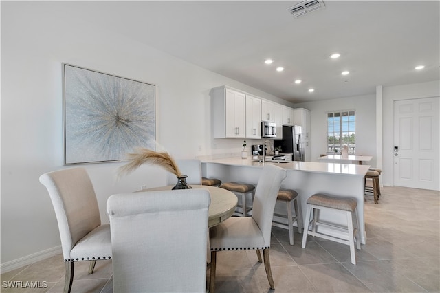 kitchen with stainless steel appliances, white cabinetry, sink, kitchen peninsula, and a kitchen breakfast bar