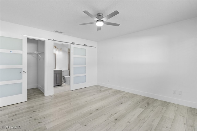 unfurnished bedroom featuring a closet, ceiling fan, a barn door, and light hardwood / wood-style floors