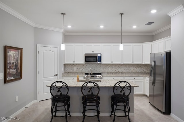 kitchen featuring appliances with stainless steel finishes, light stone counters, a kitchen island with sink, decorative light fixtures, and white cabinets