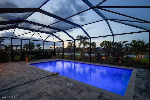 pool at dusk featuring a water view, glass enclosure, and a patio area