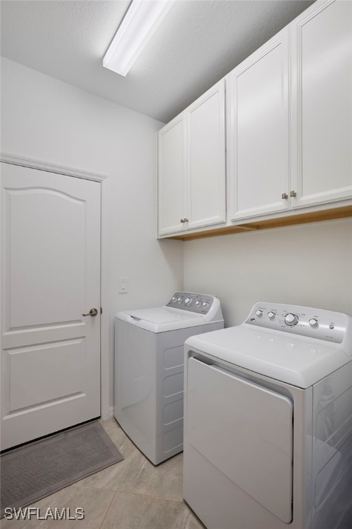 laundry room featuring independent washer and dryer, cabinets, and light tile patterned flooring