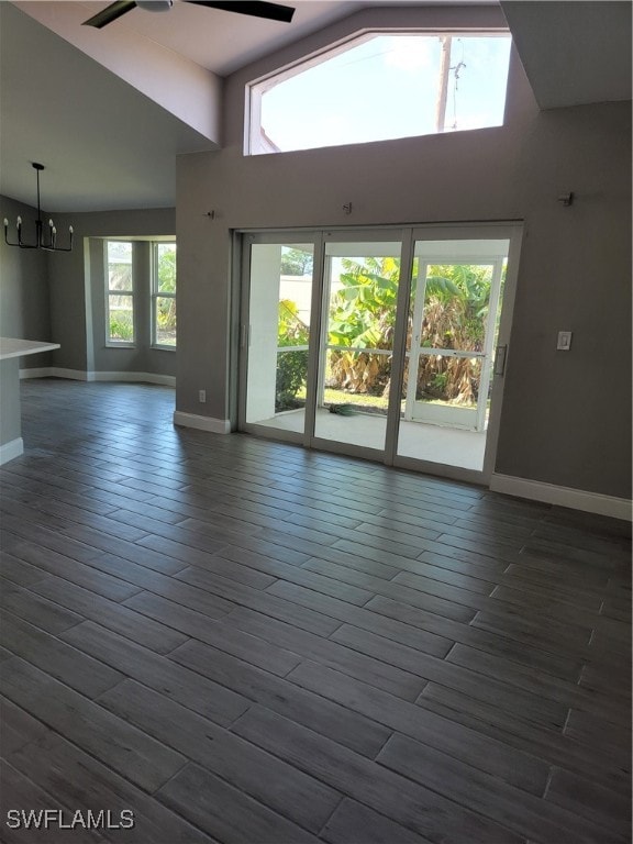 unfurnished living room with high vaulted ceiling, ceiling fan with notable chandelier, dark hardwood / wood-style floors, and plenty of natural light