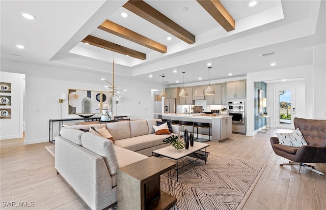 living room with light hardwood / wood-style floors, an inviting chandelier, sink, beamed ceiling, and a raised ceiling