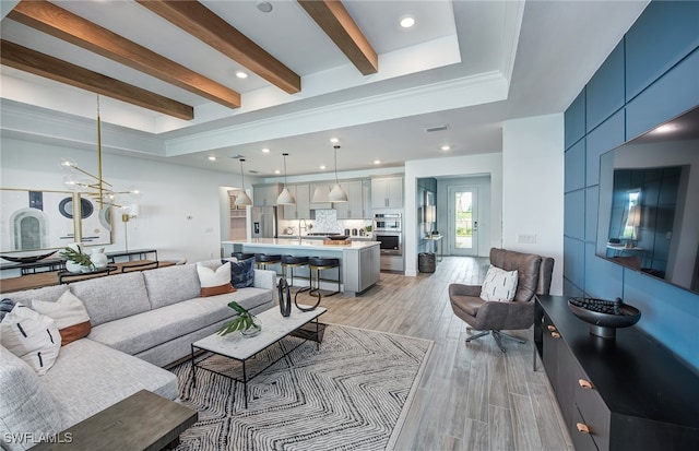 living room featuring an inviting chandelier, sink, a raised ceiling, beam ceiling, and light hardwood / wood-style flooring