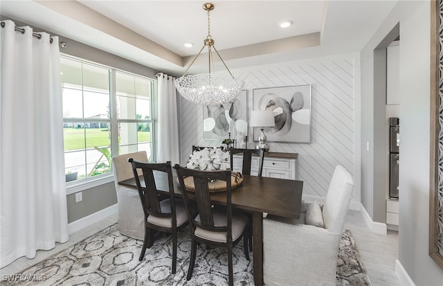 dining space with wood-type flooring, an inviting chandelier, and a raised ceiling