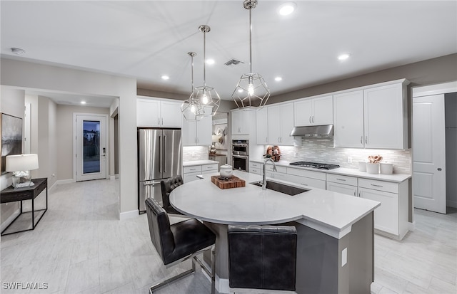 kitchen featuring a center island with sink, white cabinetry, appliances with stainless steel finishes, decorative light fixtures, and sink