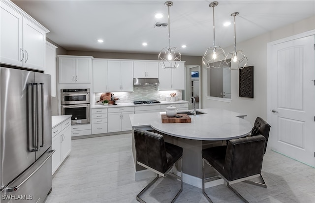 kitchen featuring white cabinets, hanging light fixtures, a breakfast bar area, an island with sink, and appliances with stainless steel finishes