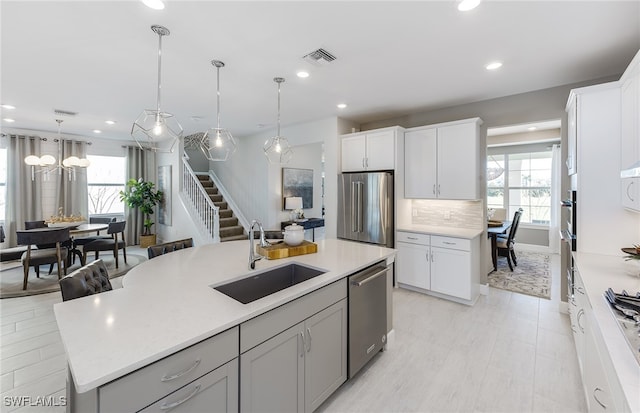 kitchen with hanging light fixtures, a wealth of natural light, a center island with sink, and appliances with stainless steel finishes