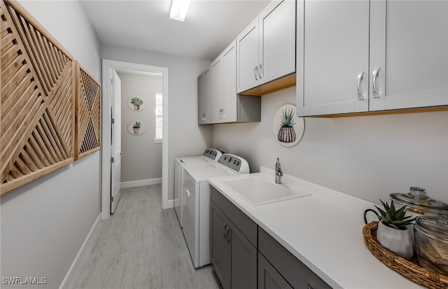 laundry room with cabinets, sink, washer and dryer, and light hardwood / wood-style flooring