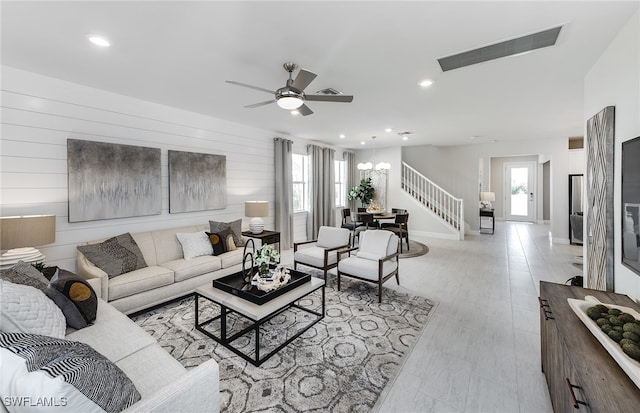 living room with ceiling fan with notable chandelier, plenty of natural light, wooden walls, and light hardwood / wood-style flooring