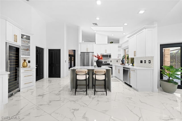 kitchen with white cabinets, a kitchen island, stainless steel appliances, and beverage cooler