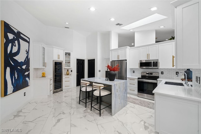 kitchen featuring white cabinetry, sink, stainless steel appliances, a high ceiling, and a kitchen island