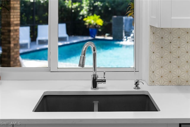 room details with tasteful backsplash, sink, and white cabinets