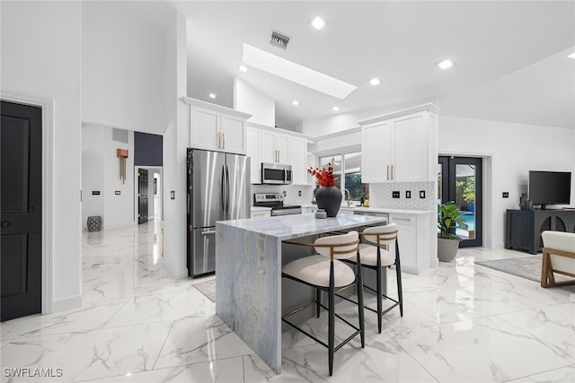 kitchen with high vaulted ceiling, white cabinets, a skylight, appliances with stainless steel finishes, and light stone counters