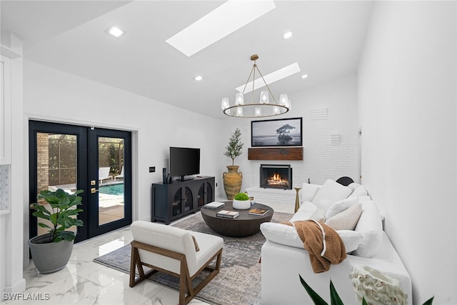 living room with a brick fireplace, lofted ceiling with skylight, french doors, and an inviting chandelier