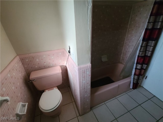 bathroom with tile patterned floors, shower / bathtub combination with curtain, tile walls, and toilet