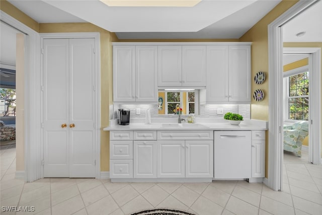 kitchen with decorative backsplash, white dishwasher, sink, light tile patterned floors, and white cabinetry